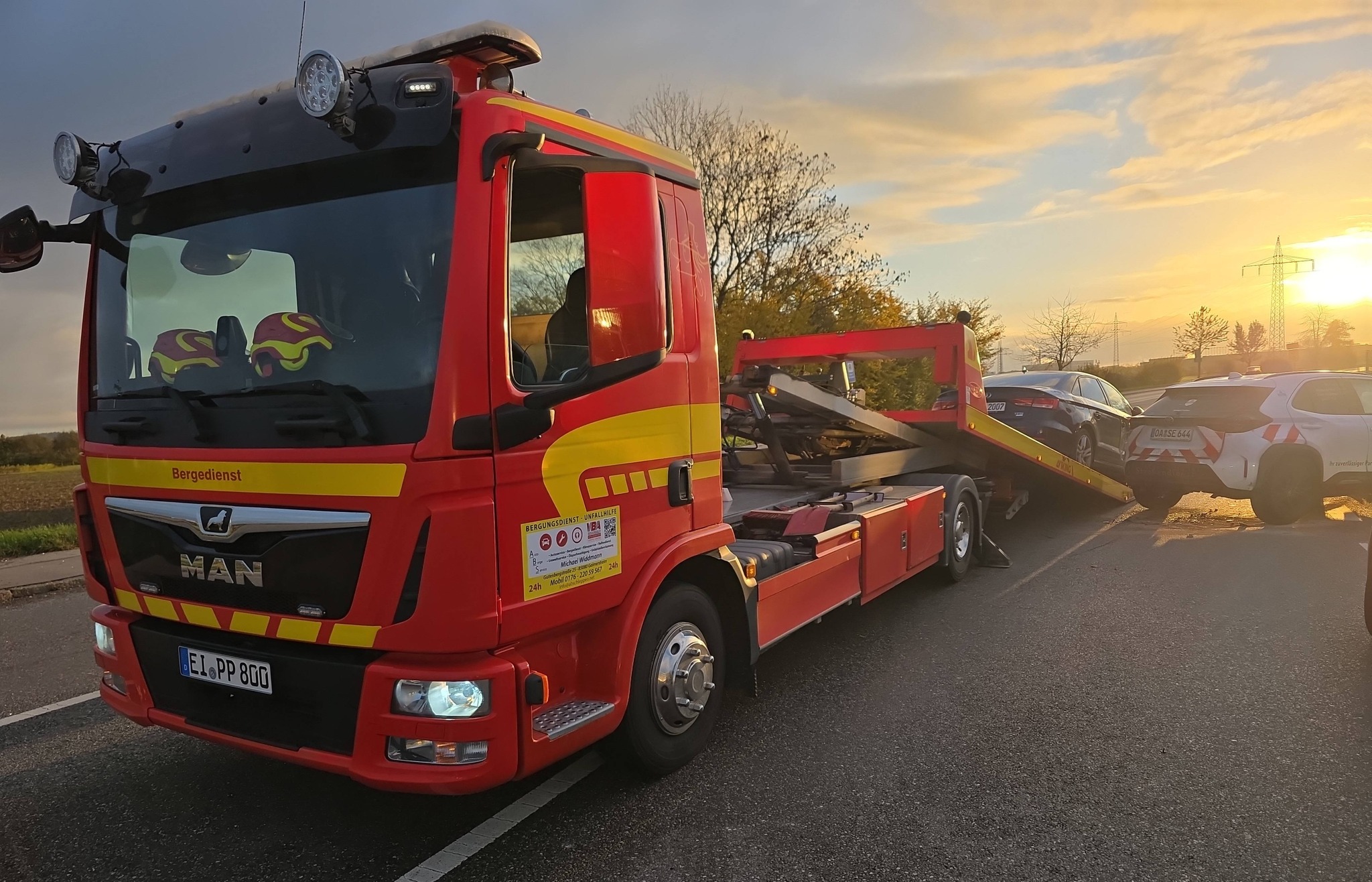 Roter MAN TGL Bergedienst bei Sonnenuntergang mit Unfallwagen auf der Ladefläche